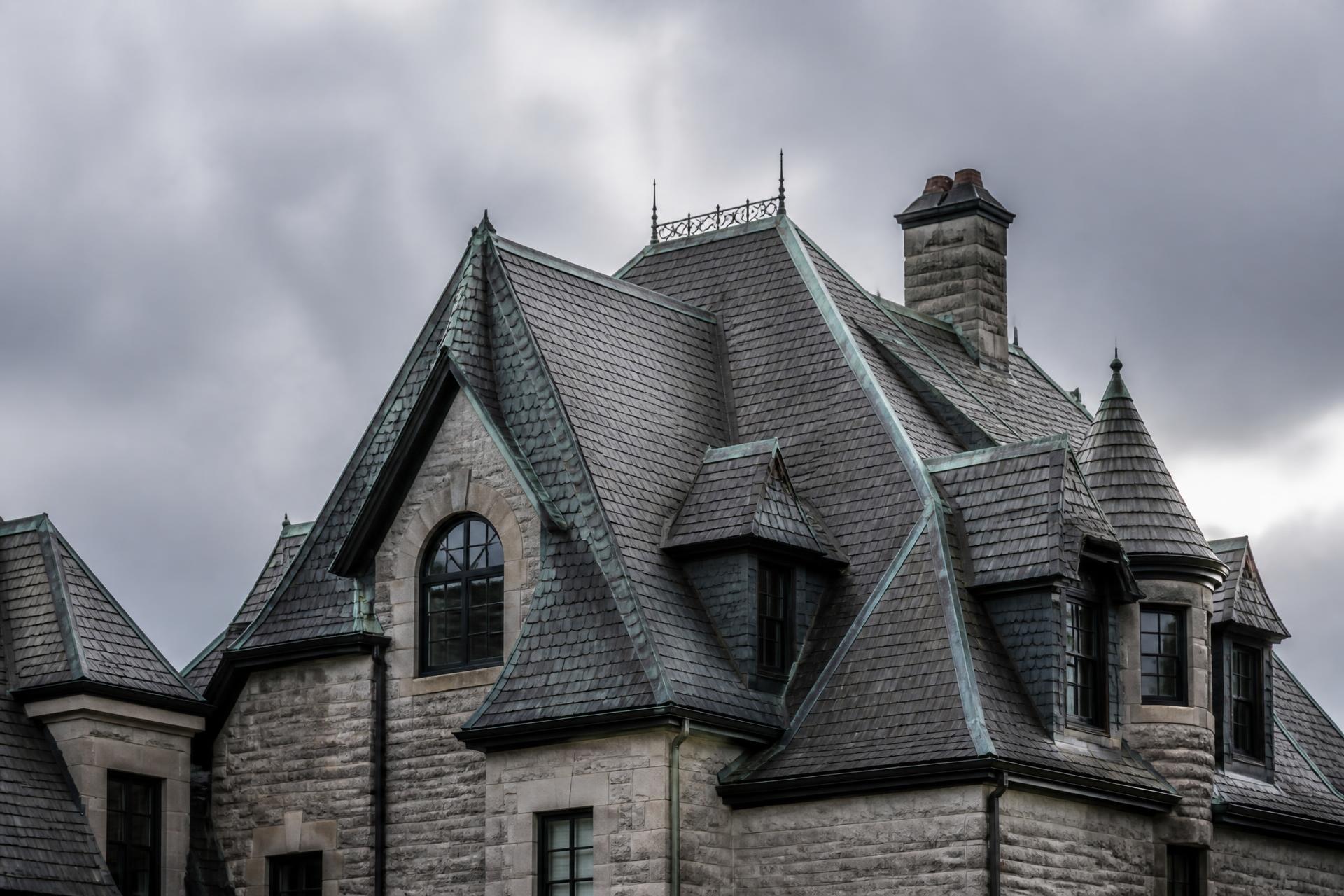 Steep slate roof of a large historic stone home under a storm sky